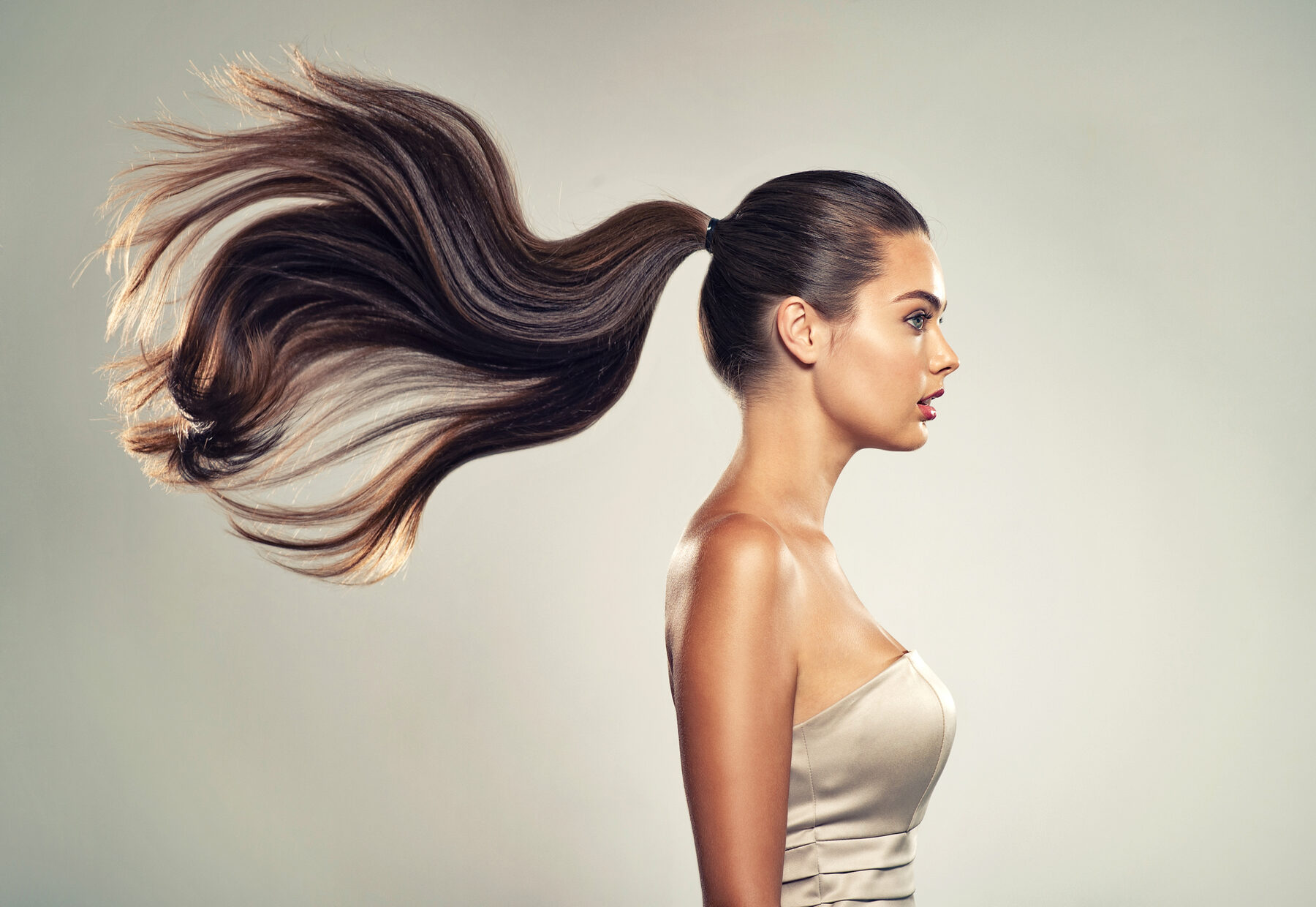 Mulher de perfil com rabo de cavalo alto e cabelo em movimento